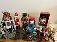 Overview of eight nutcracker figurines displayed on surface including king, Santa, bagpiper, artist, boxed, small soldier, two unfinished
