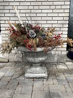 Front view of the cement planter with decorative greenery and pine cones inside, showing overall shape and detailing.