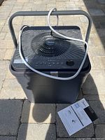 Full view of the Midea cube dehumidifier in black, showing the unit, power cord, and manual placed beside it.