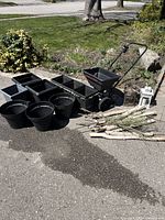 Full lot of assorted garden items arranged outdoors on pavement, showing pots, spreader, lanterns, watering can, and birch branches.