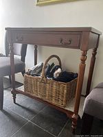 Entry table with turned legs, one drawer with metal handles, and wicker basket on lower shelf.