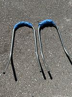 Two metal ladder jacks placed side by side on asphalt surface showing curved handles wrapped in blue tape.