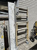 Two metal scaffold frame sections with welded rungs and one plank leaning against a brick wall