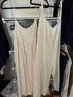 Two linen outfits hanging on a rack — one checkered dress with thin straps and the other plain cropped jumpsuit with a tied strap.