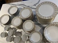 Full view of the large set of china showing stacked dinner plates, sandwich plates, side plates, fruit nappies, bowls, cups and serving pieces on a marble surface.