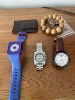 Overview of all five items spread on wood surface: three watches, bracelet, money clip