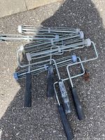Photo showing five metal 12-inch paint roller cages with black plastic handles, some with paint residue indicating used condition.