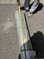 Roll of reflective bubble insulation on asphalt, being measured with a yellow tape measure showing approximately 18 feet in length.