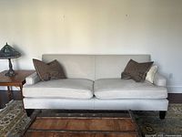 Front view of light cream chenille sofa with two large seat cushions and pillows, dark wood legs, and adjacent furniture.