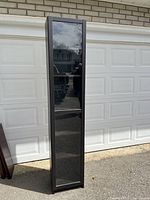 Full front view showing the tall black shelving unit with glass door closed.
