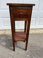 Front view of the tall wooden stand showing drawer and lower shelf.
