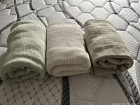 Three rolled cotton blankets in cream and green shades placed on a mattress, showing overall condition and size.