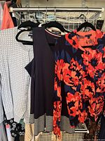 Three sweaters hanging on hangers showing the full set including floral, navy with cut out, and checkered gray sweaters.