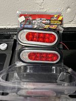 Two Fleet One combination trailer lights with red and clear lenses, in open package with visible wires and brand packaging behind.