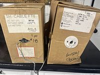 Two cardboard boxes of wire labeled Ontario Wire SH Cable FT6 and Custom Audio Video cable, showing labeling and wire feed holes.