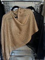 Gold and black dress shawls hanging on black hangers showing drape and fringe detail