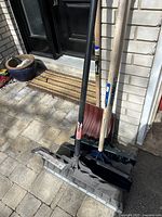 Four winter snow shovels leaning against house wall, showing wide snow pushers and traditional shovels with wooden handles.