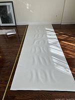 White writable and magnetic wall covering laid out on wooden floor with measuring tape along side, showing length and width.