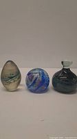 Photo of three blown glass paperweights showing overall sizes and shapes: teardrop, round swirled, and bottle-shaped with stopper.
