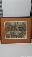 Full view of framed oil painting showing cottage scene with surrounding trees and vegetation, signature visible in lower right corner though not legible.