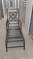 Full length front view of black metal reclining patio lounge chair outdoors in hallway with geometric patterned backrest and metal slat seat.