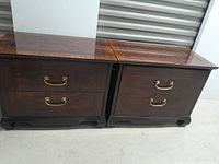 Two wooden sidetables side by side showing their front with two drawers each and brass-colored handles.