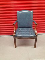 Front view of the vintage leather tufted library chair showing blue leather upholstery and wooden armrests.