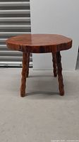 Full view of the wood log stool showing its rounded thick top and three carved legs.