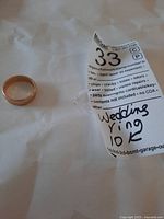 Ring and sellers tag on white background showing handwritten “Wedding ring 10K” label