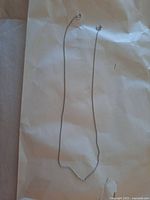 Full view of the thin white gold chain necklace laid flat on light paper.