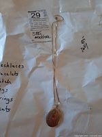 Full view of necklace hanging with oval locket pendant resting on white paper showing a tag with 925 and made in Italy markings.