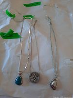 Full view of the three sterling silver necklaces laid out separately on white paper with green tape labels.