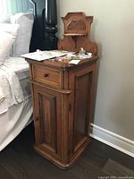 Side view of antique wooden night table cabinet next to bed, shows overall structure and finish.