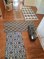Four area rugs laid out on hardwood floor, showing varying colors, patterns, and lengths