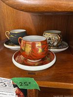 Front view showing all three teacups with their respective saucers on a wood shelf.
