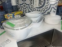 CorningWare white and floral baking dishes grouped on kitchen counter, including white bowls, casserole dishes, and glass lids