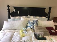 Full bed view with all linens, pillows, comforter, afghan, bunny toy arranged on bed with black wooden headboard.