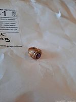 Front angled view of ring on paper backdrop showing purple stone and engraved text around bezel