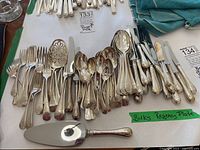 Overview of flatware set laid out on table showing forks, spoons, knives and a pie server with a green label reading 'Birks Regency Plate'