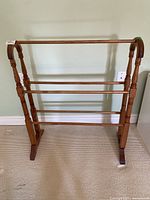 Front view of the wooden blanket stand showing three horizontal rails and turned legs.