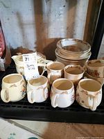Six mugs in front, stacked bowls and pitcher behind on shelf