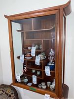 Front view showing overall cabinet with glass door, curved shelves and decorative top and bottom edges.