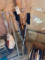 Photo showing multiple walking canes and poles leaning against a wall including a gray adjustable height cane, a wooden cane, and others.
