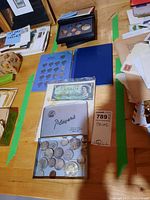Overall view of various coins, a silver 1967 centennial dollar, a blue coin album with incomplete nickel coins, 1988 proof coin set in black case, and a 1967 $1 Canadian bill