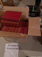 Box of multiple hardcover books with red bindings labeled 'DICKENS COLLECTION' in hand-written note