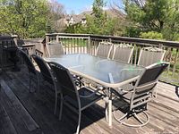 Wide view of eight chairs around rectangular glass-top table on wooden deck