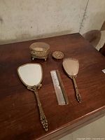 Entire dresser set laid out on wooden surface showing mirror, brush, comb, jewellery box, trinket box, and metal dish.