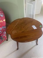 Wooden drop leaf side table with one leaf raised, showing the curved top and three legs