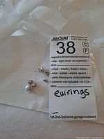Two pairs of sterling silver stud earrings placed on top of a plastic bag with a MaxSold tag labeled 'earrings'. The pearl stud earrings have a decorative silver rim; the other pair are simple round sterling silver studs.