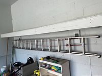 Full view of aluminum extension ladder mounted on wall in garage, showing its length and condition.